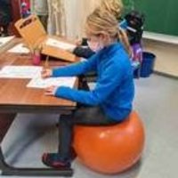 Mädchen sitzt auf orangenem Gymnastikball am Schreibtisch