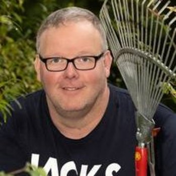 lächelnder Mann mit Laubharke in der linken Hand