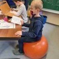 Junge sitzt auf orangenem Gymnastikball am Tisch